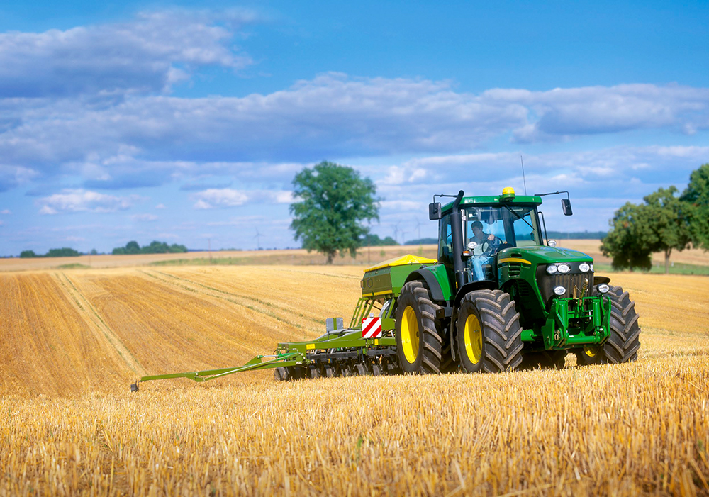 A tractor plowing a field of crops on a sunny day.