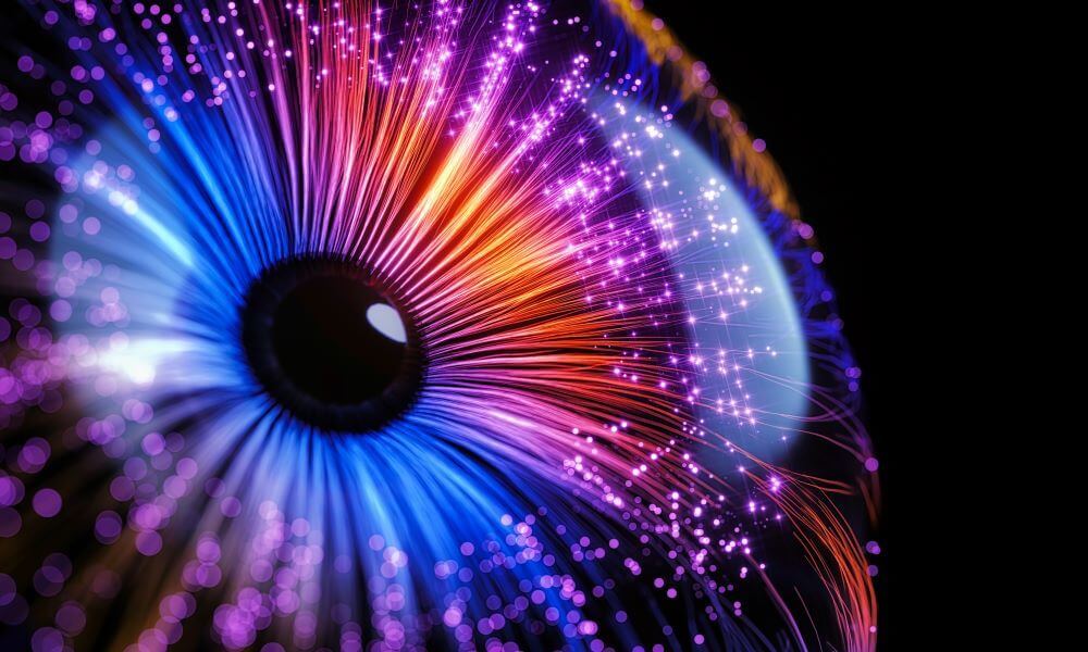 Close-up of a stylized eye, with radiating strands of light in shades of blue, purple, orange, and pink. The effect is luminous and abstract.