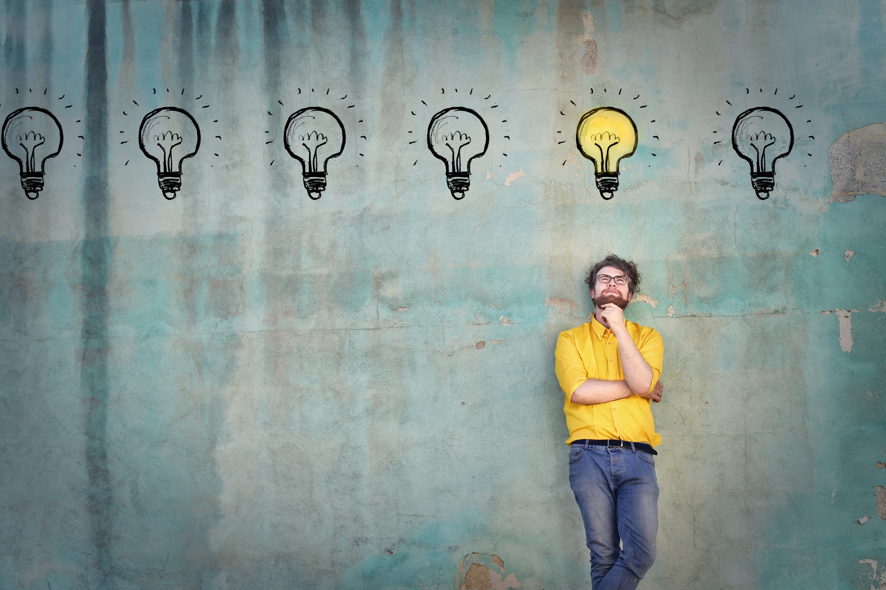 Photograph of a man standing under an illustration of a light bulbs with one lightbulb illuminated over his head